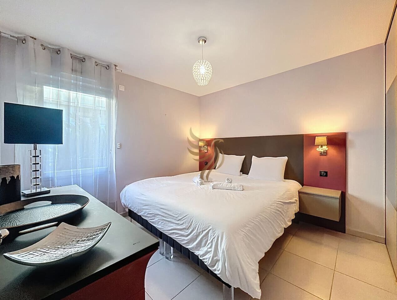 A hotel room with a bed, bedside lamps, a desk with a lamp, and a decorative light fixture.