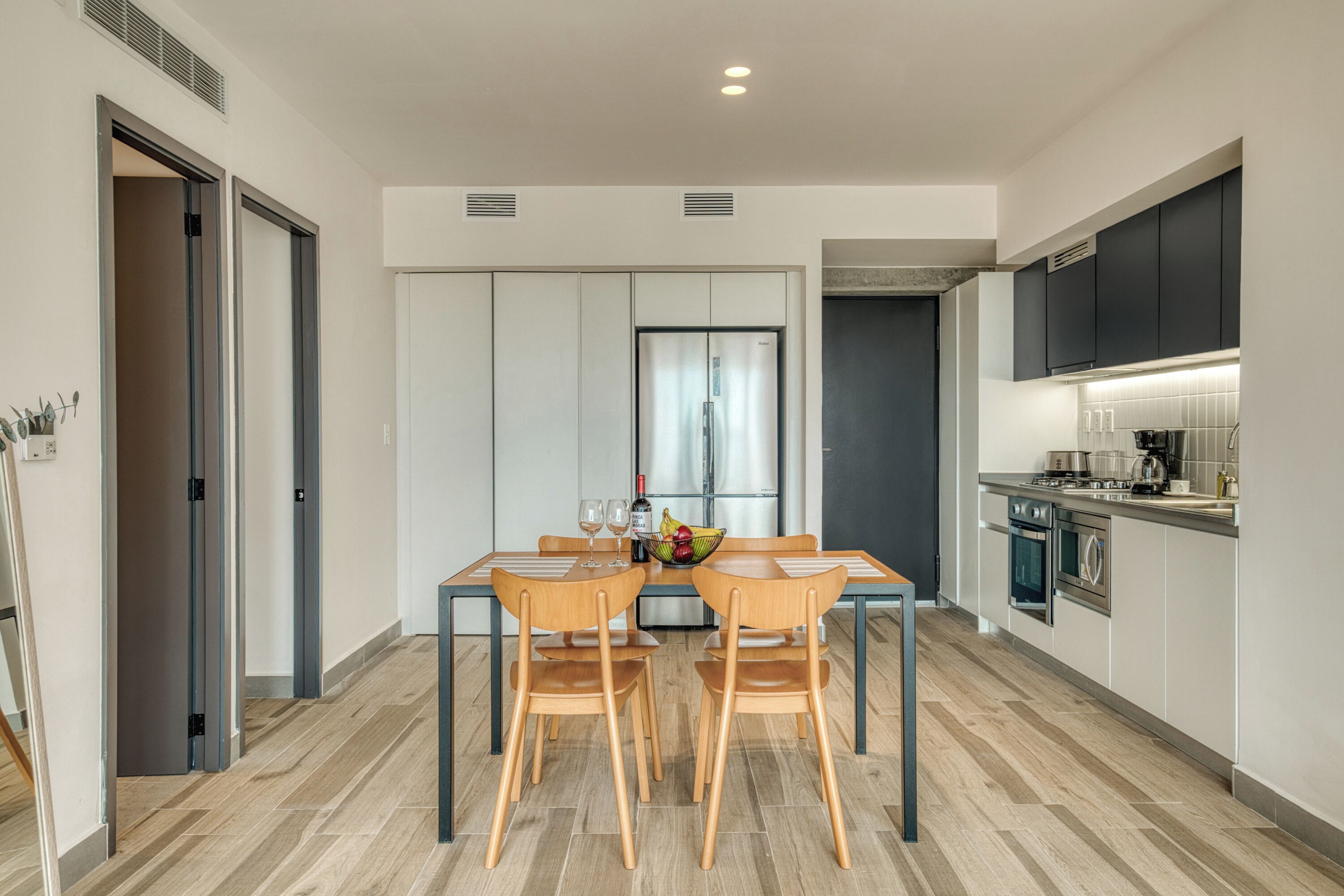 A modern kitchen with a dining area, featuring a stainless steel refrigerator, a stove, and a sink.