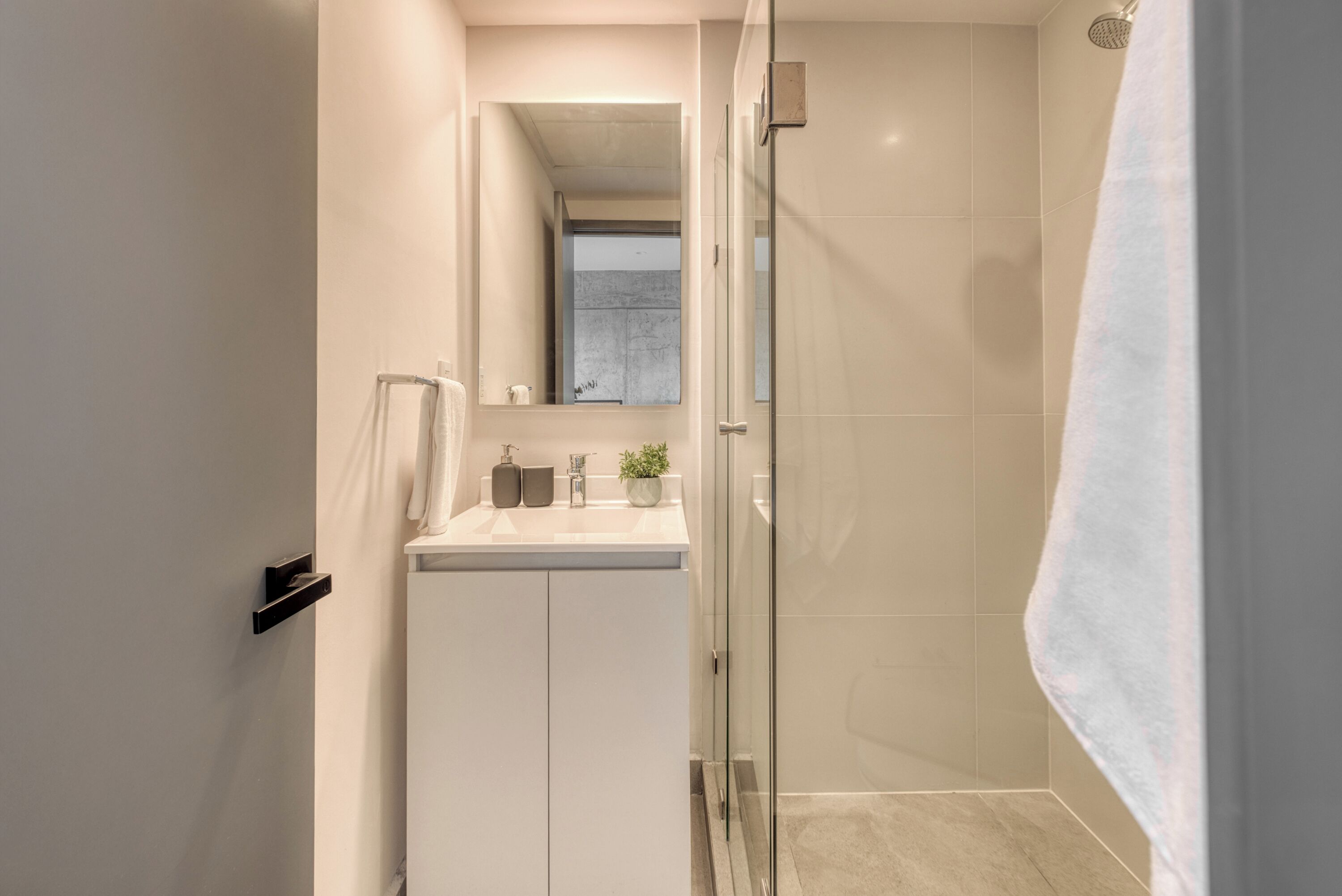 Une salle de bain moderne avec une douche à l’italienne en verre, un lavabo blanc avec un miroir au-dessus, et une serviette accrochée au mur.