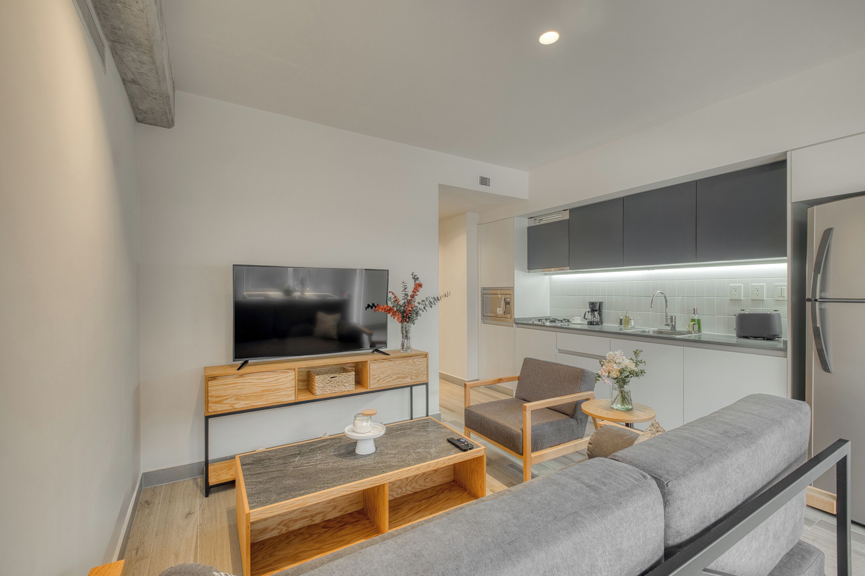 A modern living room with a flat-screen TV, wooden furniture, and a grey sofa.