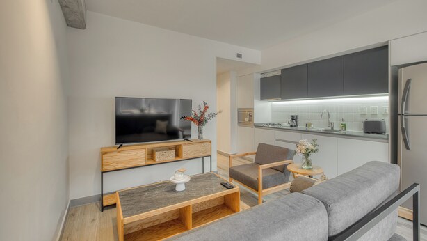 Een moderne woonkamer met een flatscreen televisie, houten meubels en een grijze bank.