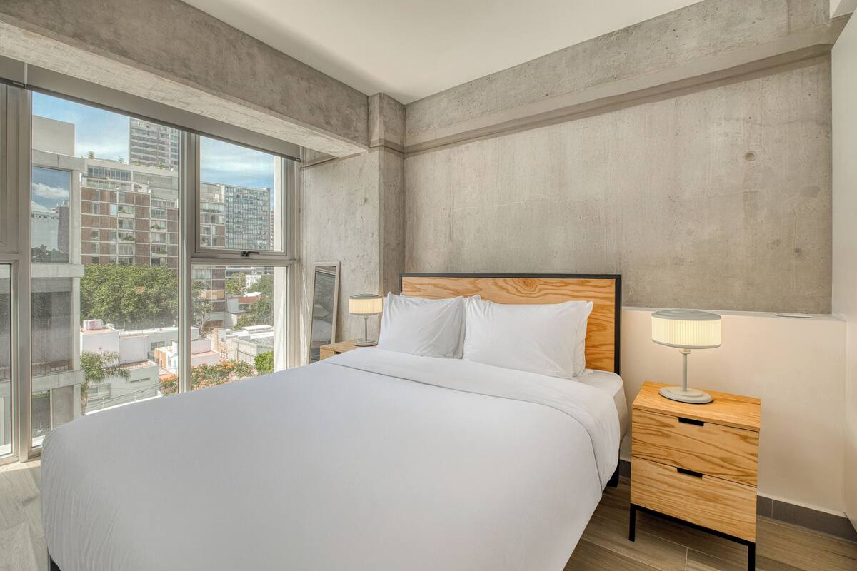 Une chambre à coucher moderne avec un grand lit, une tête de lit en bois et une table de chevet avec une lampe.