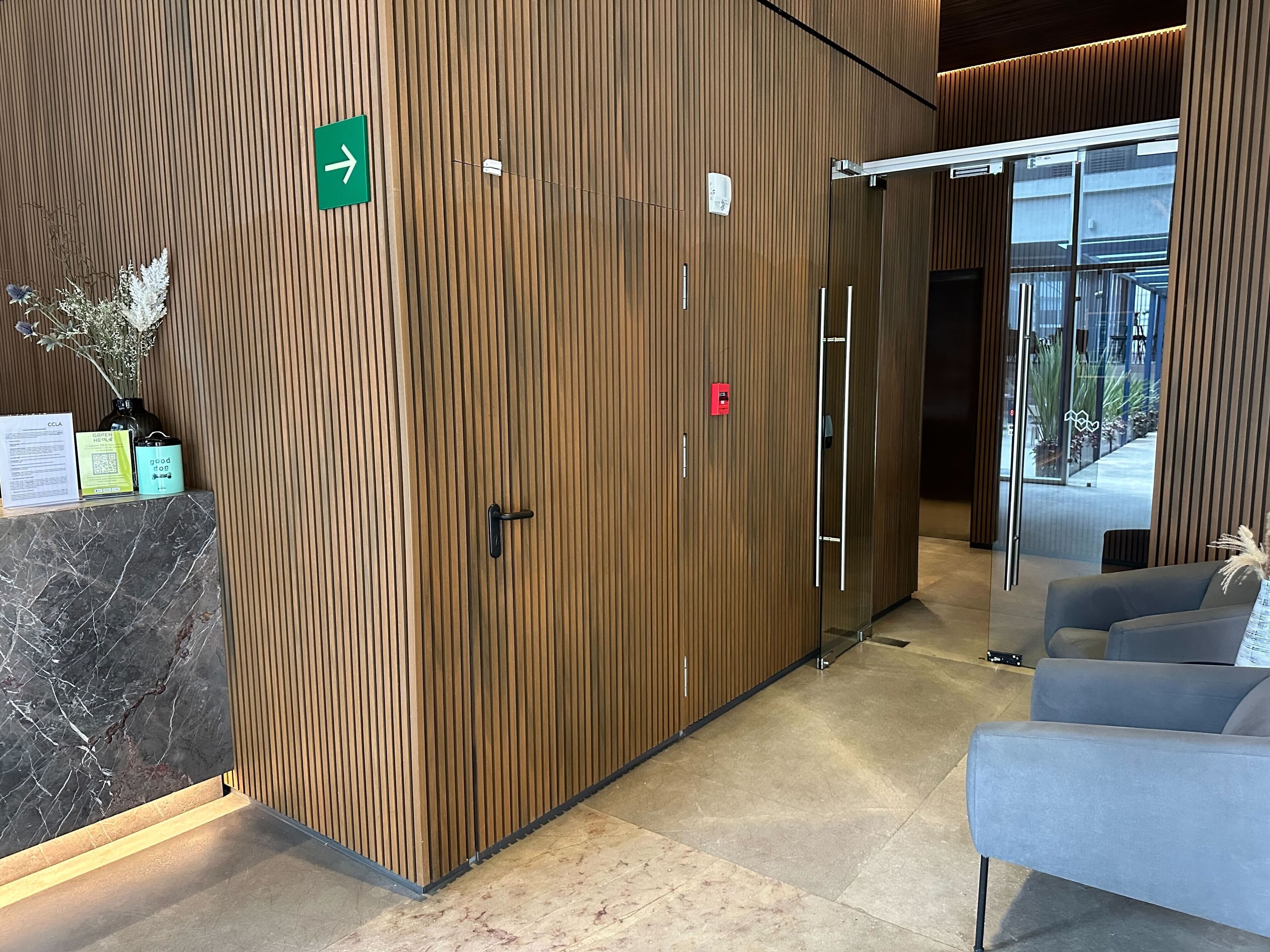 A modern reception area with a wooden panel wall, a reception desk with a marble top, and a grey sofa.