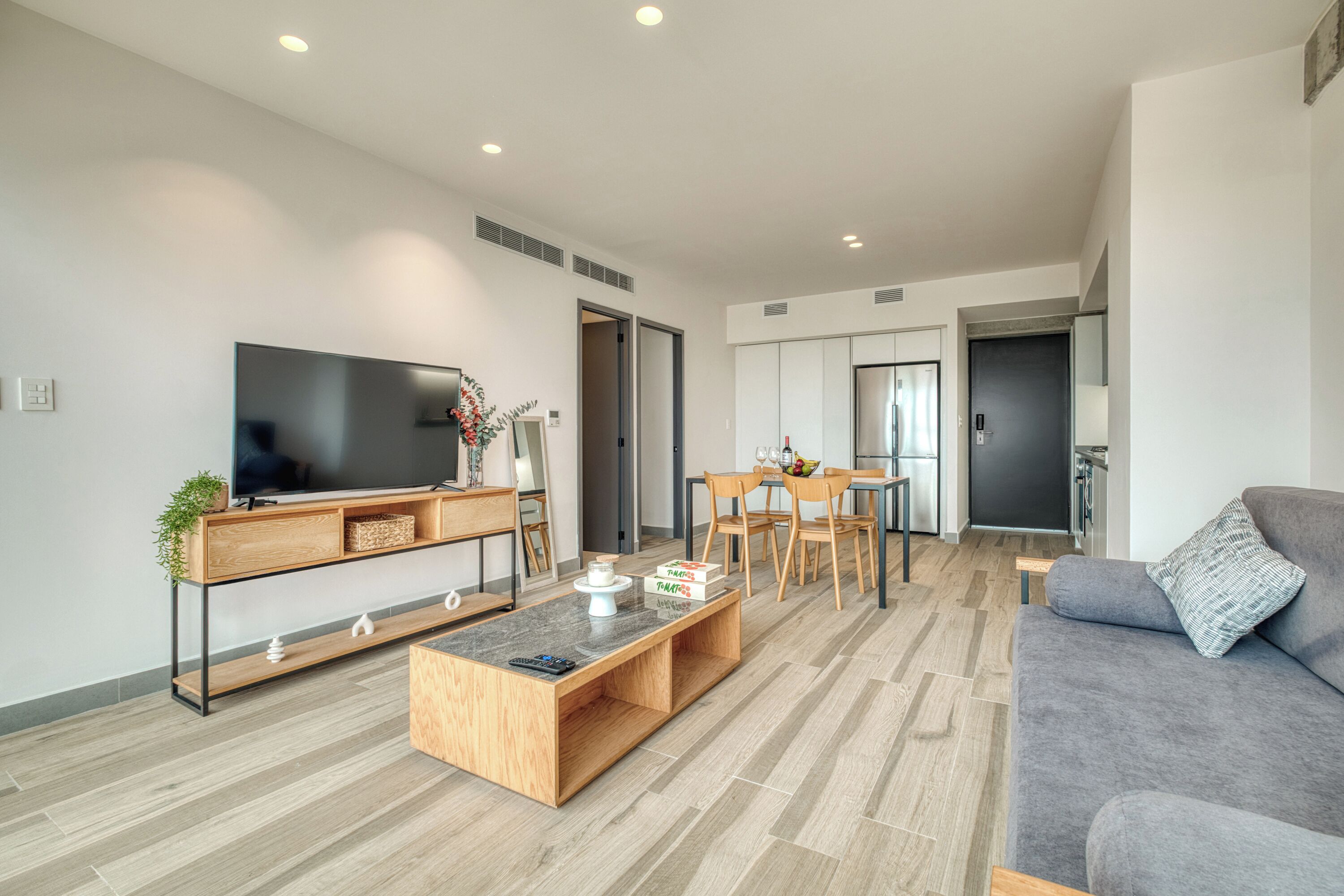 Un salon moderne doté d’un téléviseur à écran plat, d’une table basse en bois, d’un canapé gris et d’un coin repas avec des chaises et une table.