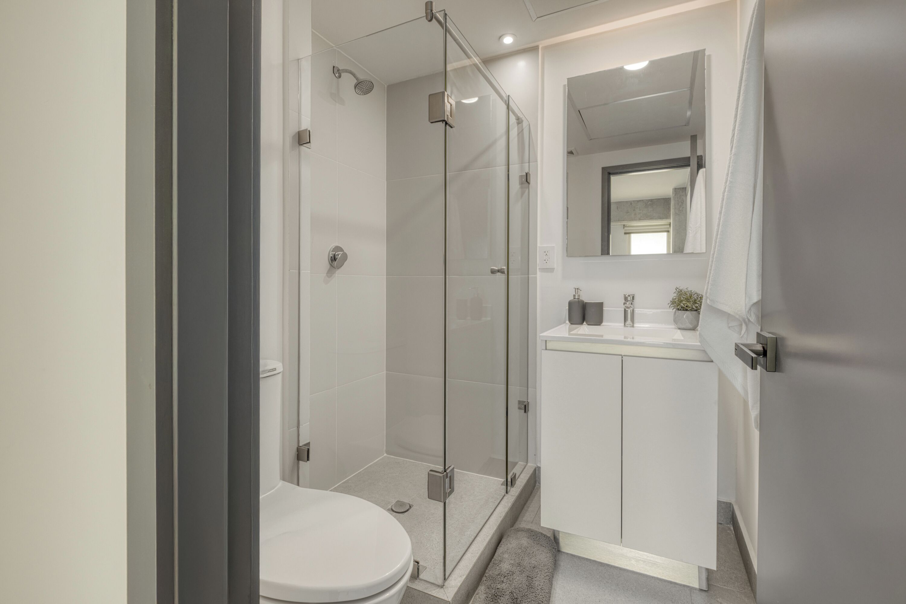 Un baño moderno con ducha envuelta en vidrio, inodoro blanco y tocador con espejo.
