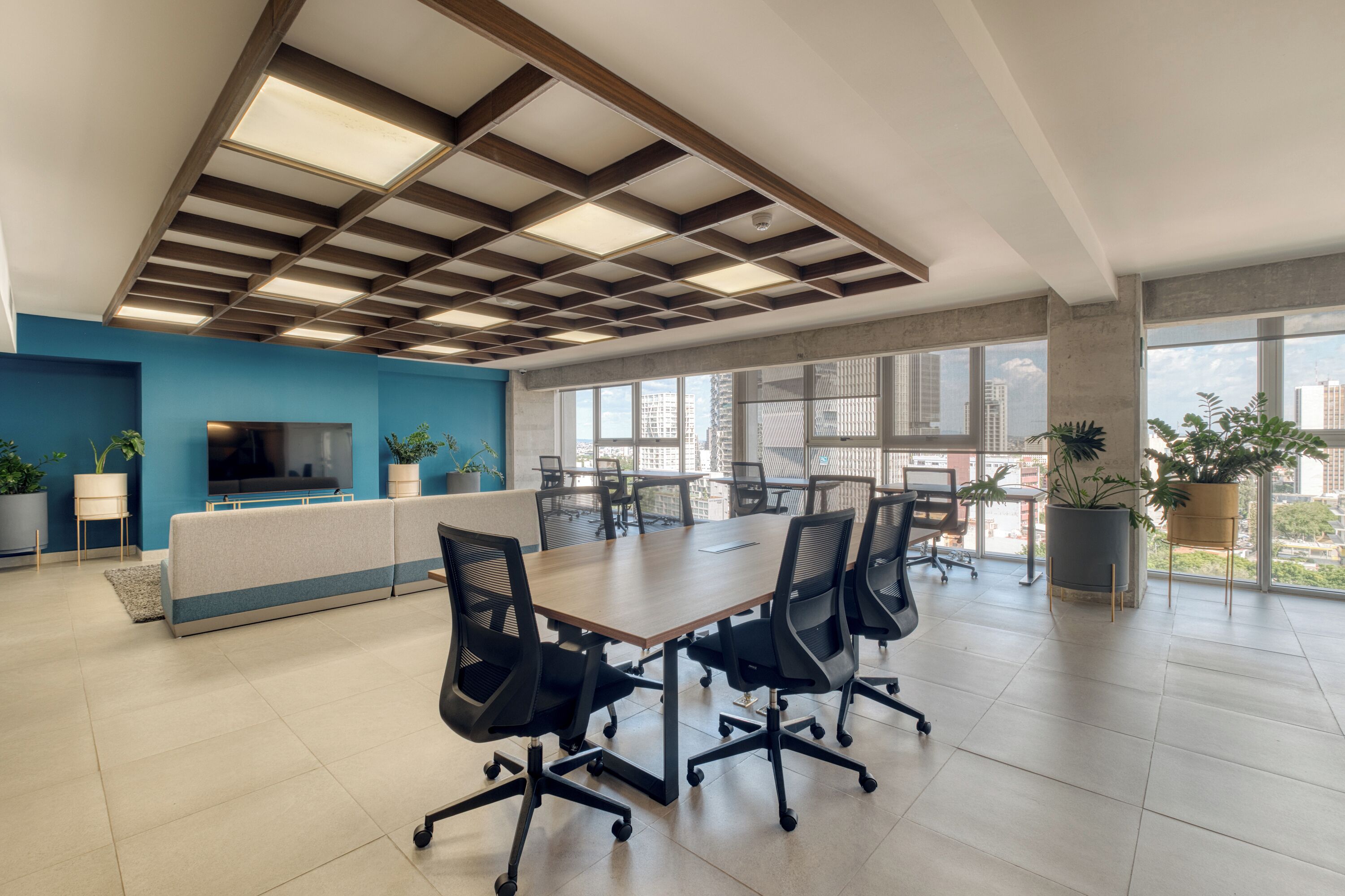 Un espace de bureau moderne doté d’une grande table de conférence, de chaises ergonomiques, d’un mur d’accent bleu et de grandes fenêtres offrant une vue sur la ville.