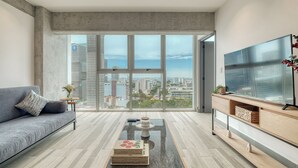 Een moderne woonkamer met een groot raam, een bank, een salontafel en een tv op een houten standaard.