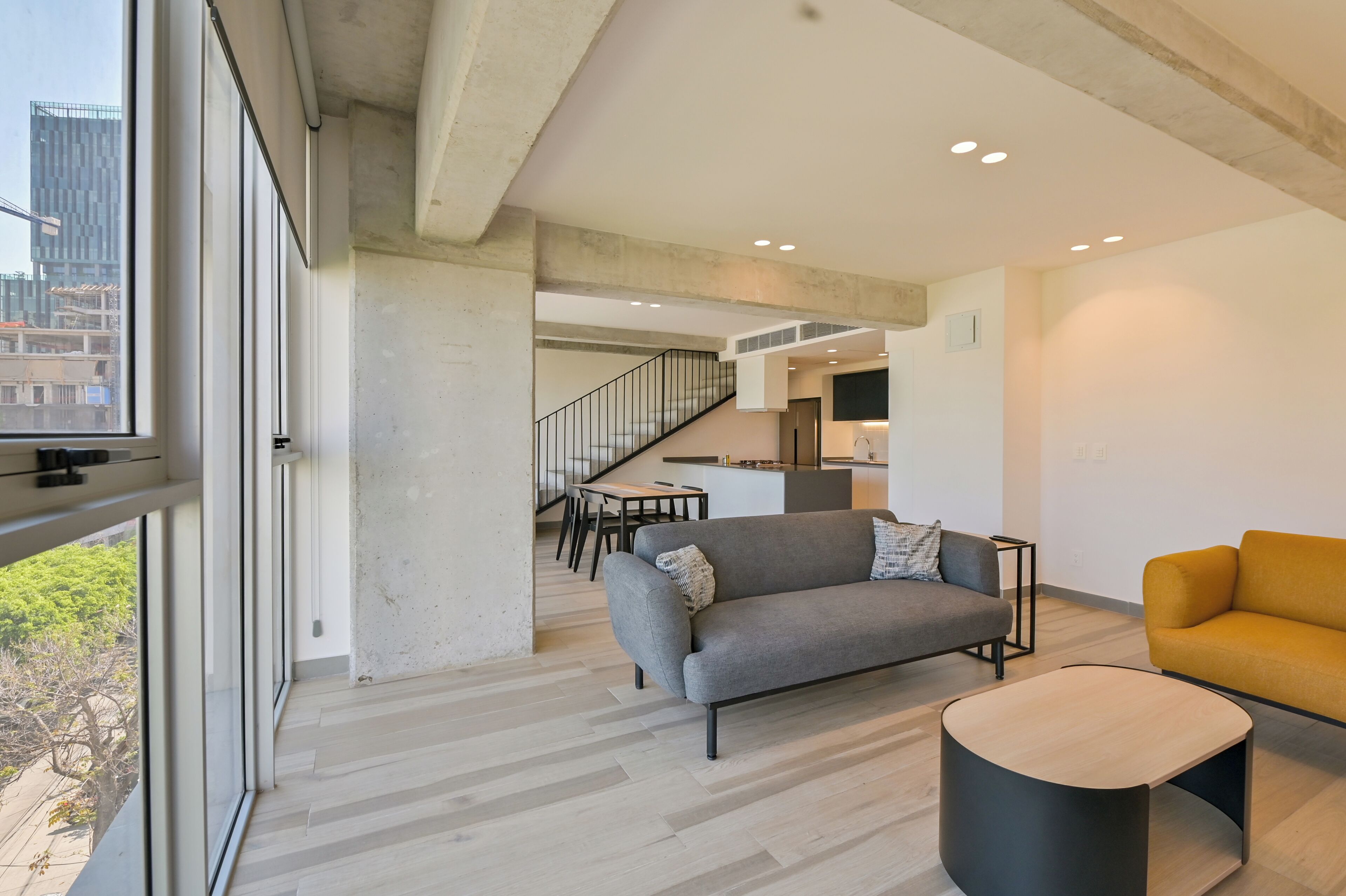 A modern living room with a sofa, a coffee table, and a view through large windows.