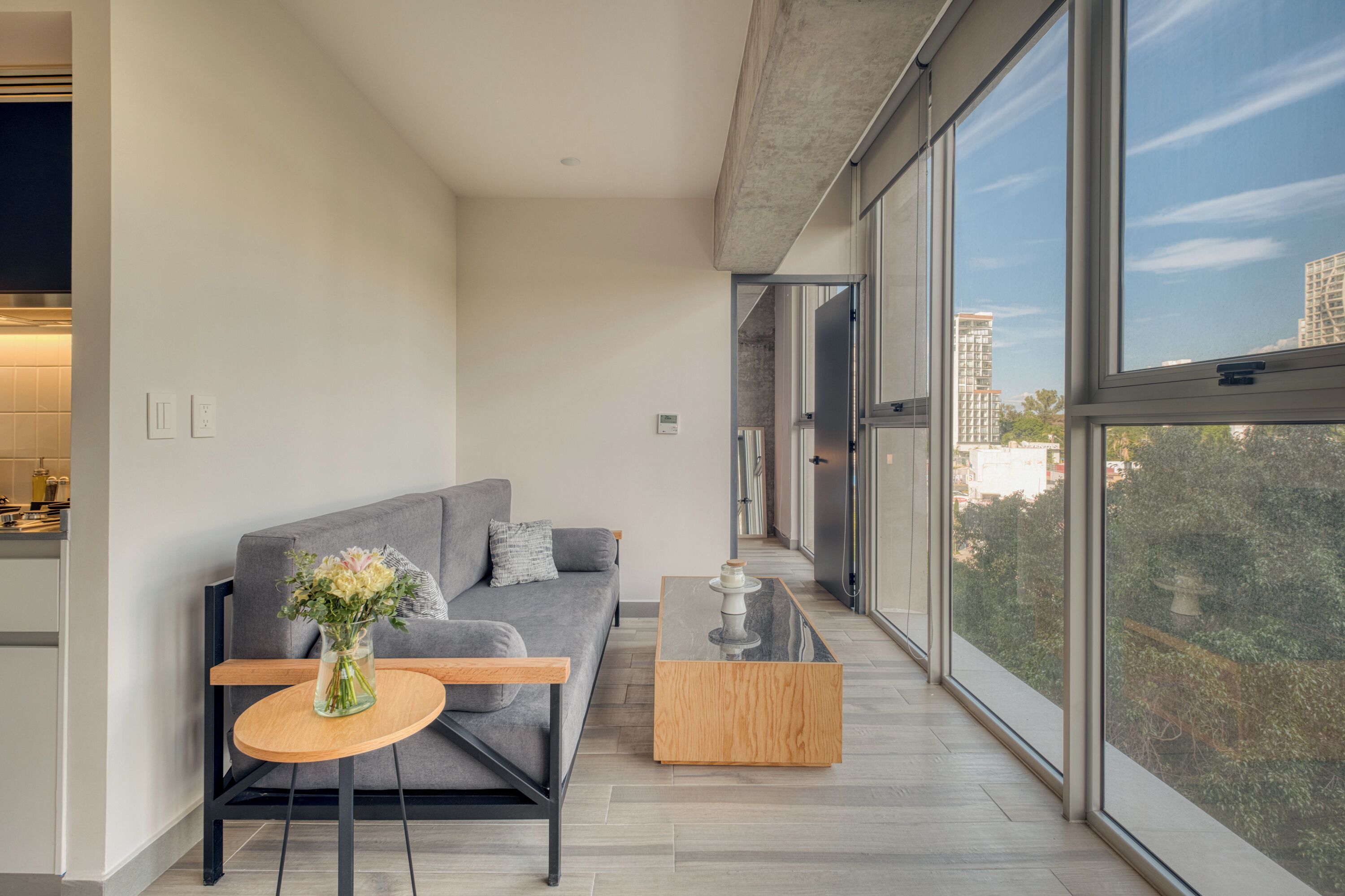 Un salon moderne avec un canapé gris, une table basse ronde en bois et un vase de fleurs.