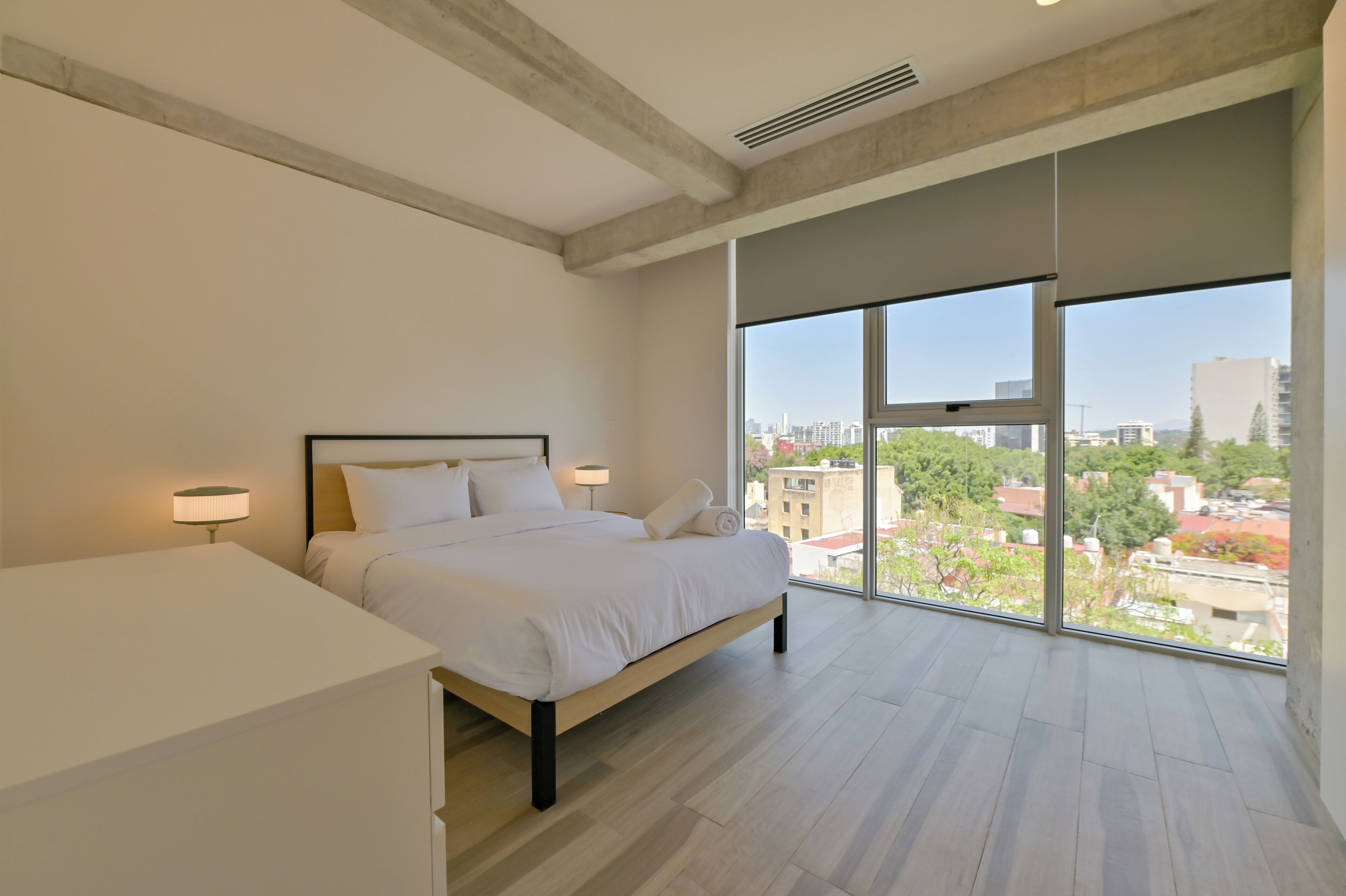 A bedroom with a large window, a bed, and a bedside table.