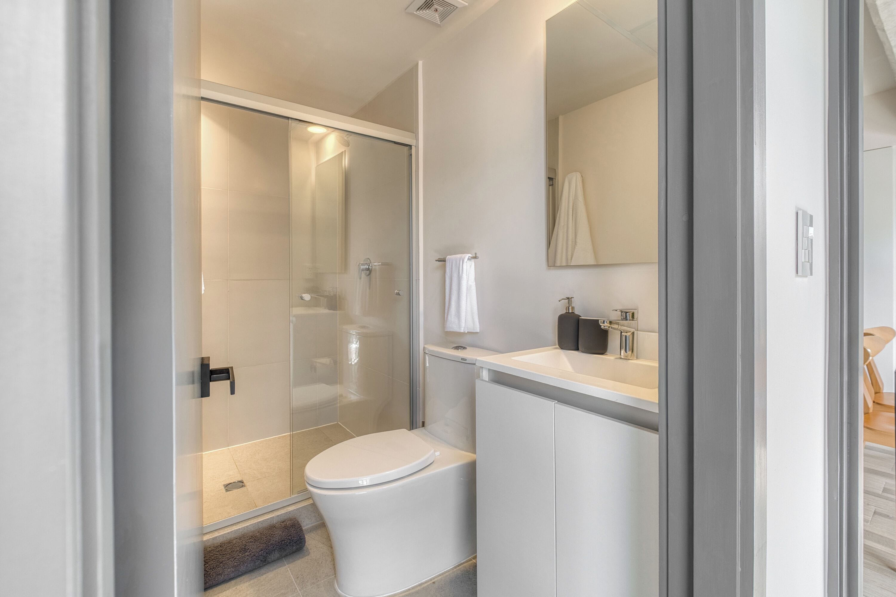 Une salle de bain moderne avec une douche à parois de verre, des toilettes blanches et un lavabo avec un miroir au-dessus.