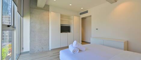 A modern hotel room with a large bed, a walk-in closet, a television, and a view of greenery outside.