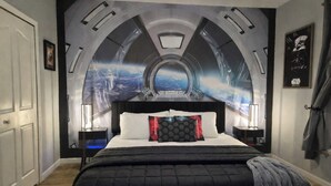Ein Schlafzimmer mit einem großen Bett, einem Kopfteil mit einem runden Fenster und einem Wandbild, das eine futuristische Stadt zeigt.