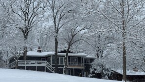 Una casa cubierta de nieve con una escalera que lleva a una terraza, rodeada de árboles.