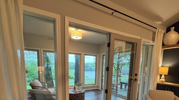 Habitación con puerta corrediza de vidrio que da a una terraza exterior con vista a un lago y vegetación.