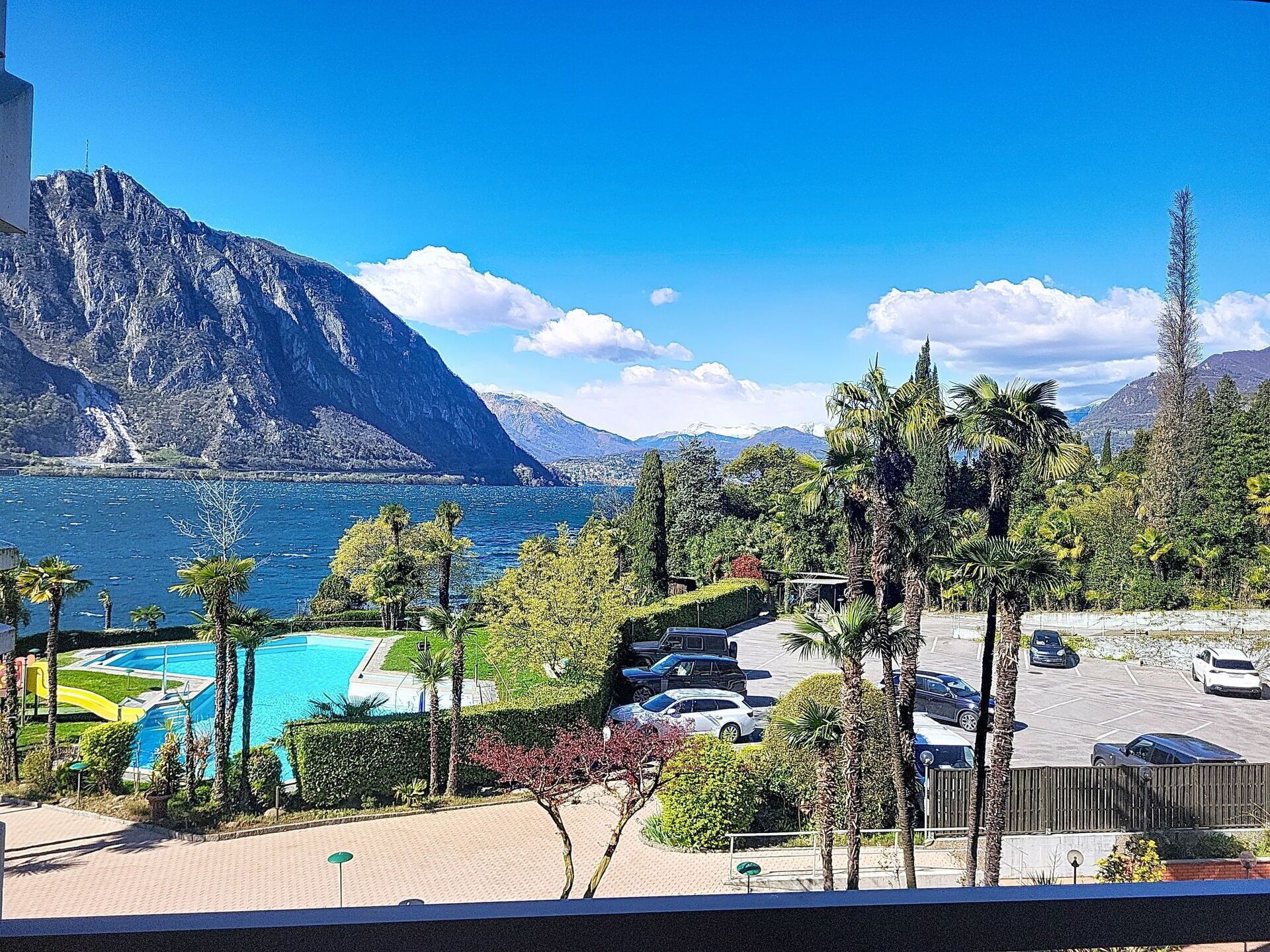 Une vue sur un paysage montagneux avec un plan d’eau, une piscine et des voitures garées.
