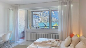 Un dormitorio con cama, una silla, un ventanal con vistas a montañas y agua, y un ventilador de techo.