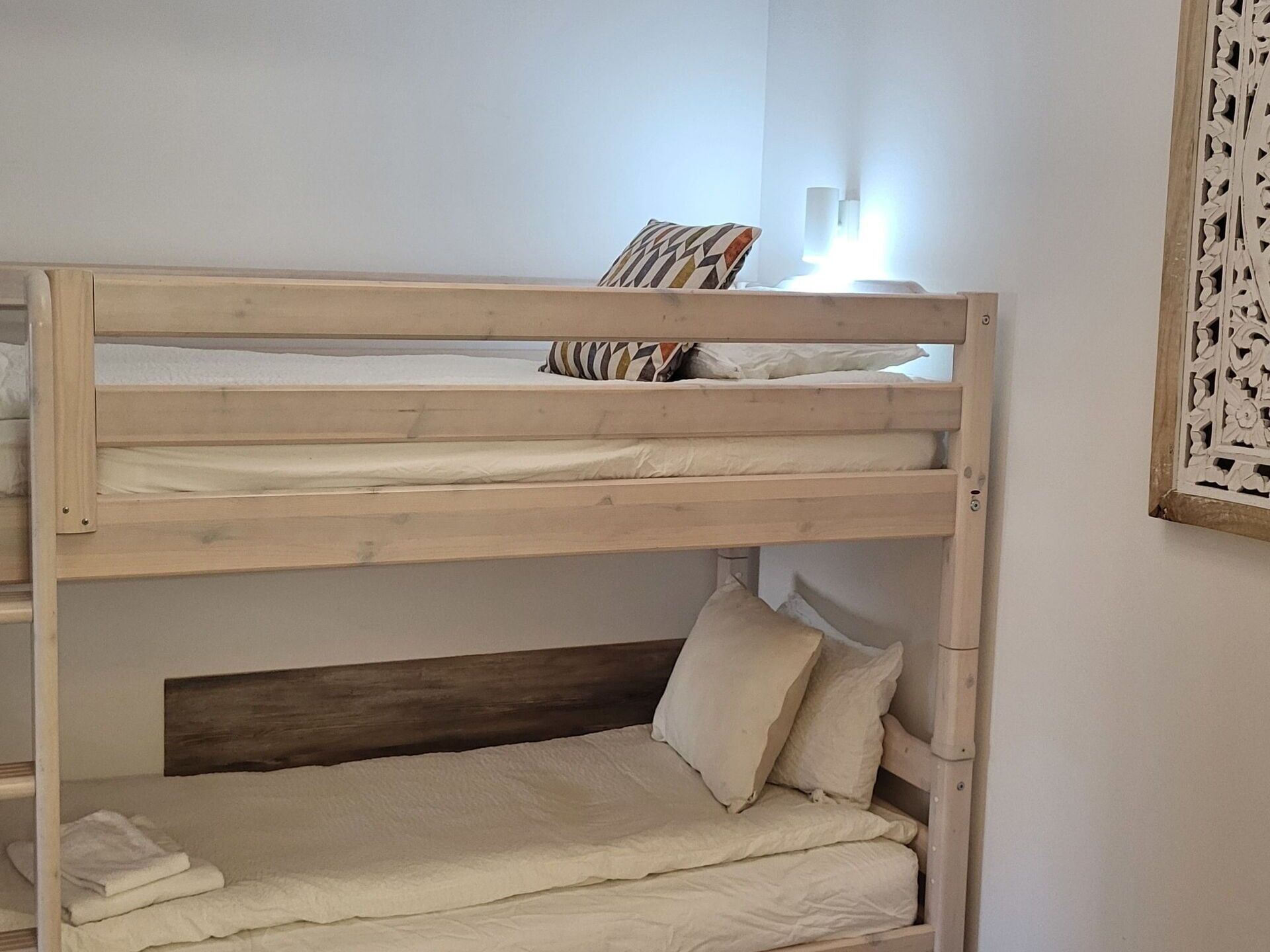 A bunk bed with two levels, a wooden headboard, and a wall-mounted light fixture.