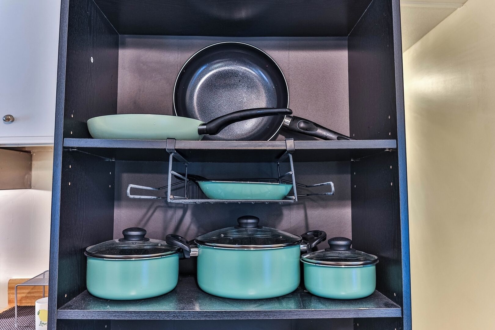 A kitchen with a black countertop, a teal pot rack, and a black frying pan on the shelf.
