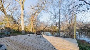 Eine Holzterrasse mit einer Bank bietet Blick auf ein Gewässer, umgeben von Bäumen.