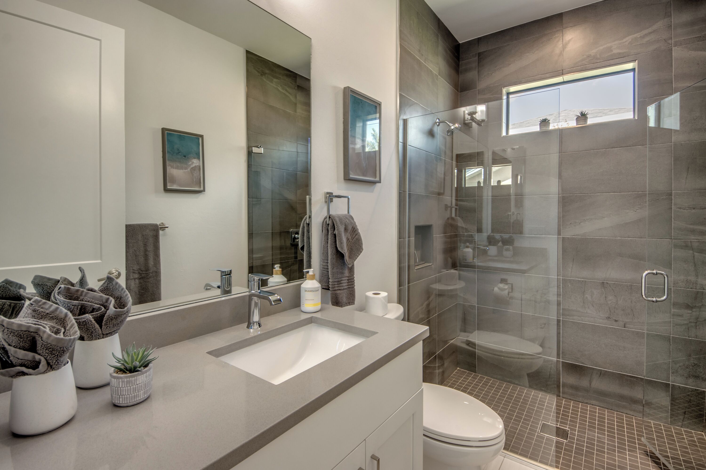 Une salle de bain moderne avec un grand miroir, un lavabo, des toilettes et une douche à parois de verre.