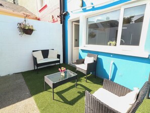 Eine Terrasse mit einer Couch, zwei Stühlen, einem Glastisch und Kunstgrasanlage.