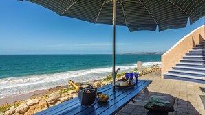 Una terraza frente al mar con una mesa preparada para una comida, una botella de champán y vistas al océano.