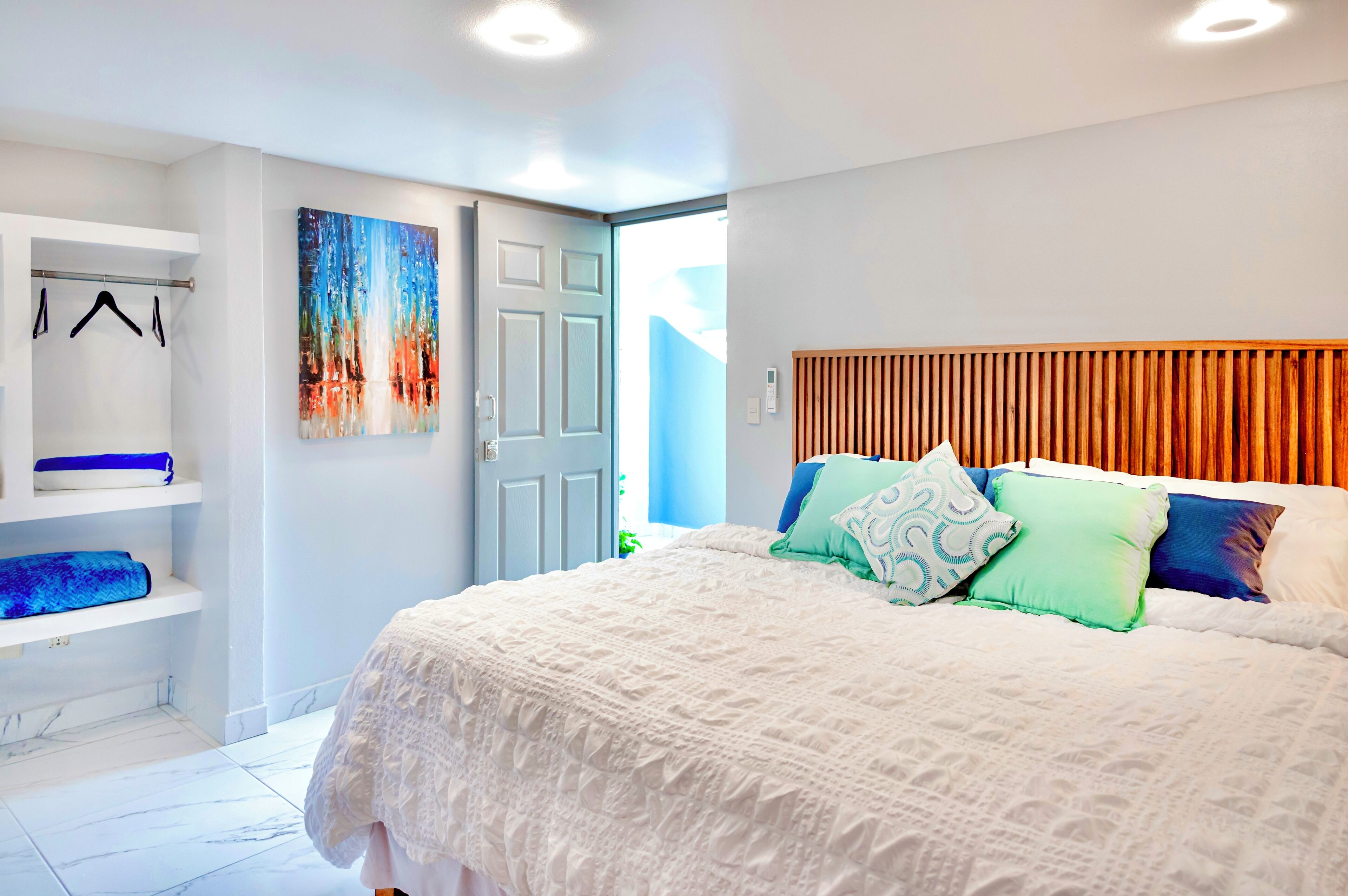 Un dormitorio con una cama grande, un armario, un cuadro en la pared y una puerta que da a otra habitación.