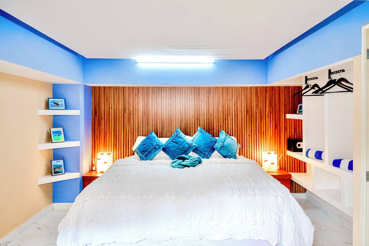 Una camera da letto con un letto, cuscini blu, una testiera in legno ed elementi a scaffale fissati al muro.