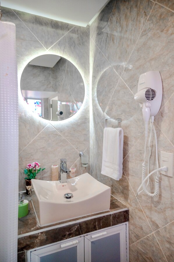 Une salle de bain équipée d’un lavabo, d’un miroir, d’un sèche-cheveux et d’un porte-serviettes.