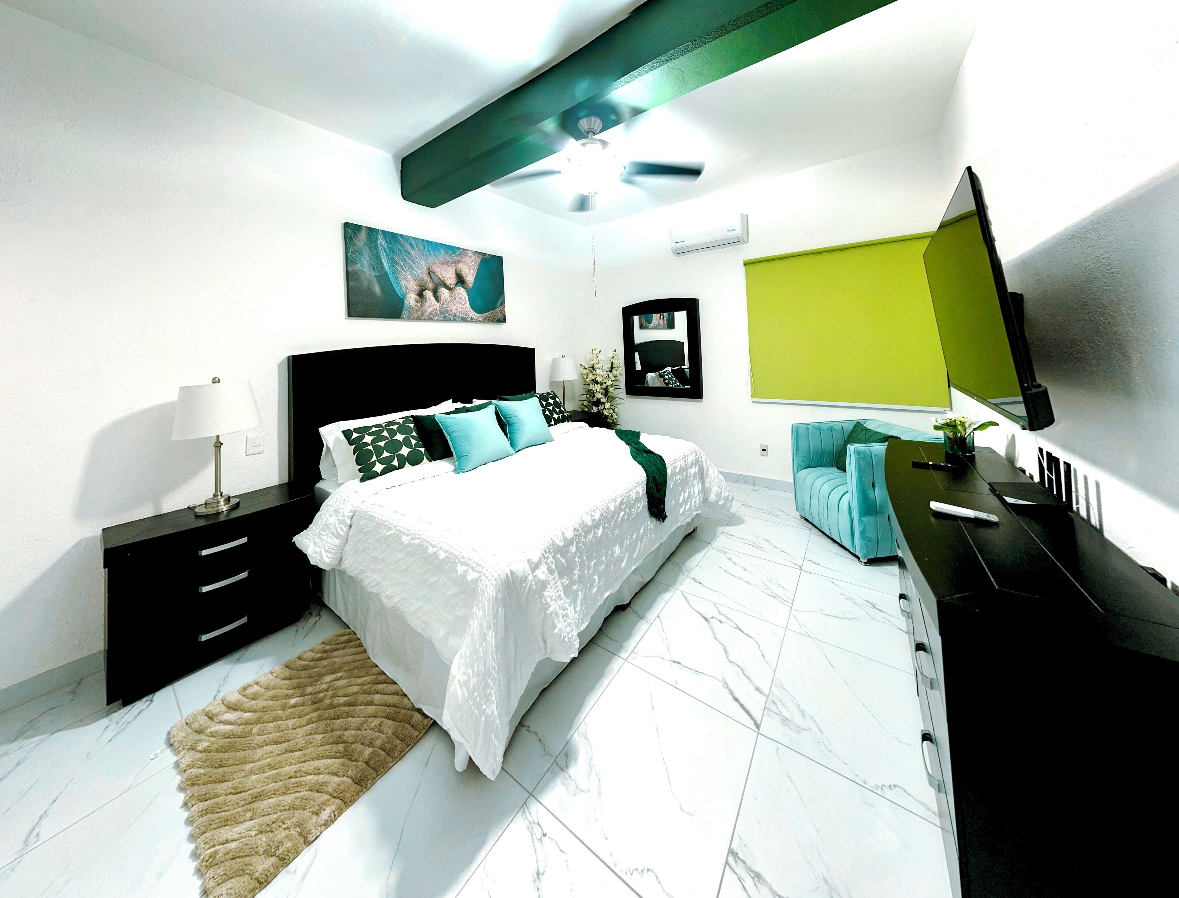 A modern bedroom with a bed, a desk, a chair, a TV, and a painting on the wall.