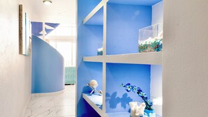 Interior azul e branco com uma escadaria curva, piso de mármore e prateleiras com objetos decorativos.