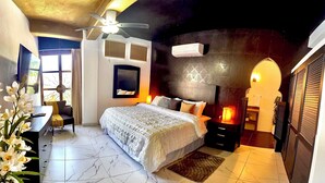 Quarto com cama, escrivaninha, cadeira, ventoinha no teto, janela e aparelho de ar condicionado.
