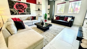 Uma sala de estar moderna com um sofá bege, um sofá preto e uma mesa de centro. Há um quadro grande de uma rosa na parede, e um vaso de planta no canto.