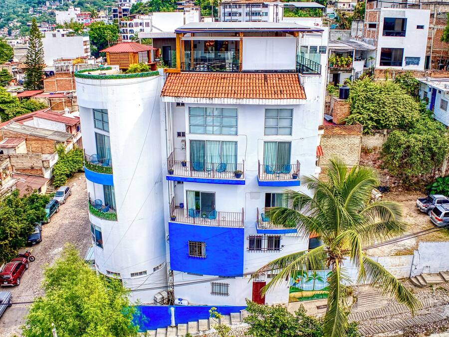 Um edifício de vários andares com varandas, telhado de telhas vermelhas e entorno urbano.