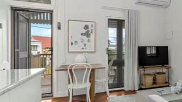 Ein modernes Wohnzimmer mit Holzboden, einem weißen Sofa, einem Fernseher und einem Essbereich mit weißem Tisch und Stühlen.