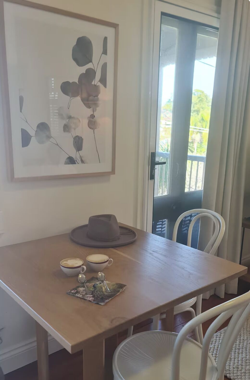 A dining area with a wooden table, two white chairs, a hat, two cups, and a small decorative item.