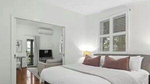 Ein Schlafzimmer mit Bett, Nachttisch, einem Fenster mit Jalousien und einer Tür, die auf einen Balkon führt.