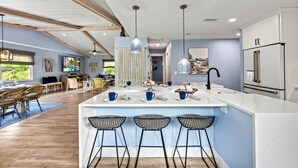 Una cocina moderna con una isla central, taburetes de bar, luces colgantes y un refrigerador.