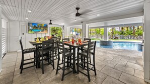 Un patio cubierto con piscina, mobiliario exterior y una pantalla de televisión.