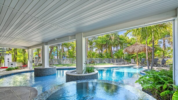 Una piscina con borde de azulejos, rodeada de sillas de descanso y palmeras.