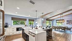 Una cocina moderna con una isla grande, armarios blancos y un comedor con sillas y una mesa de madera.