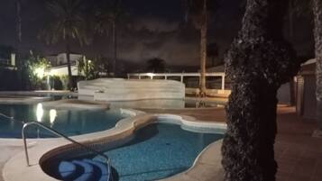 A swimming pool with a curved design, surrounded by a tiled deck and palm trees.