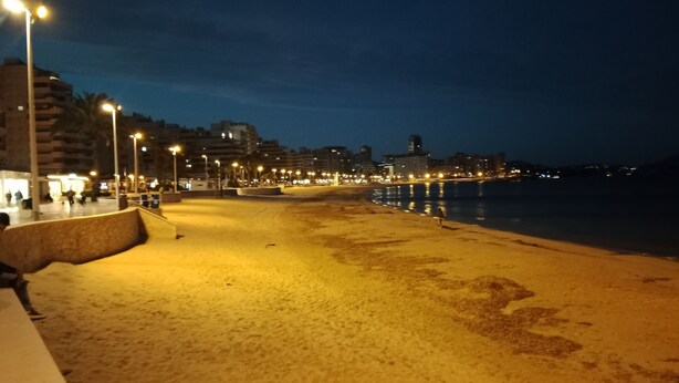En strand i natt med gatlyktor och byggnader i bakgrunden.