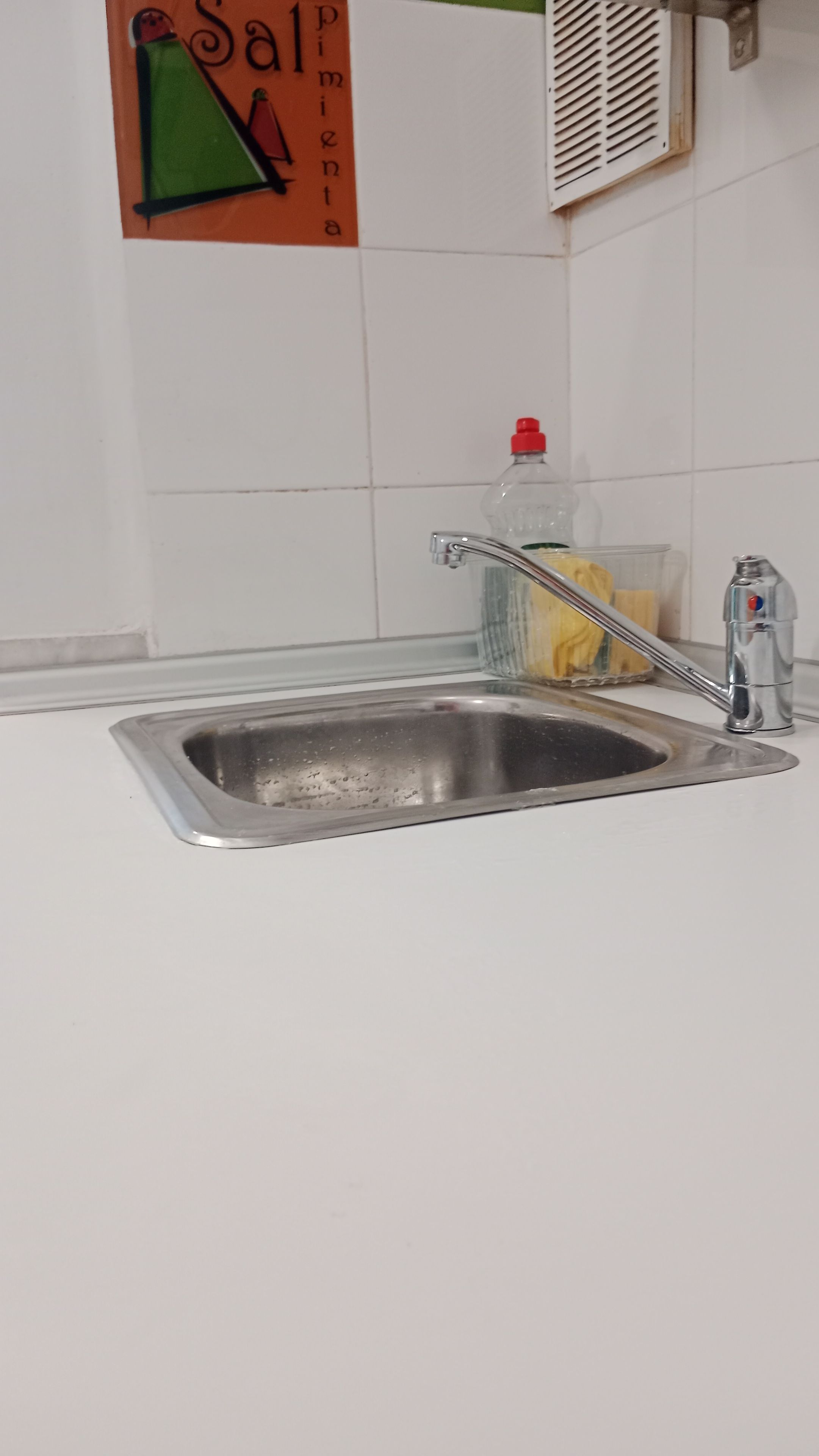 Un évier de cuisine avec un robinet, une bouteille de liquide vaisselle et une éponge.