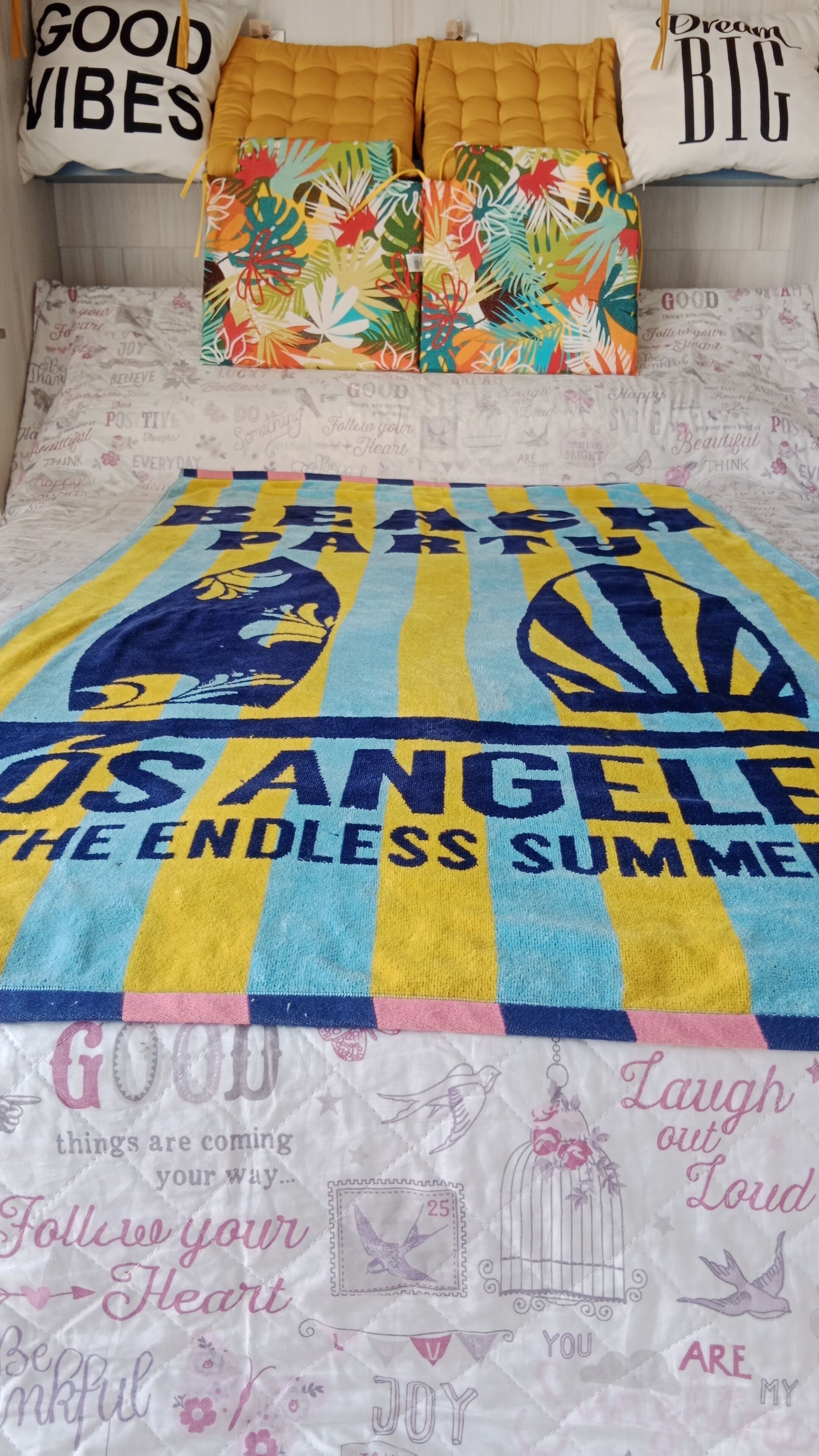 A bed with a colorful blanket featuring motivational phrases and a pillow with a similar design.