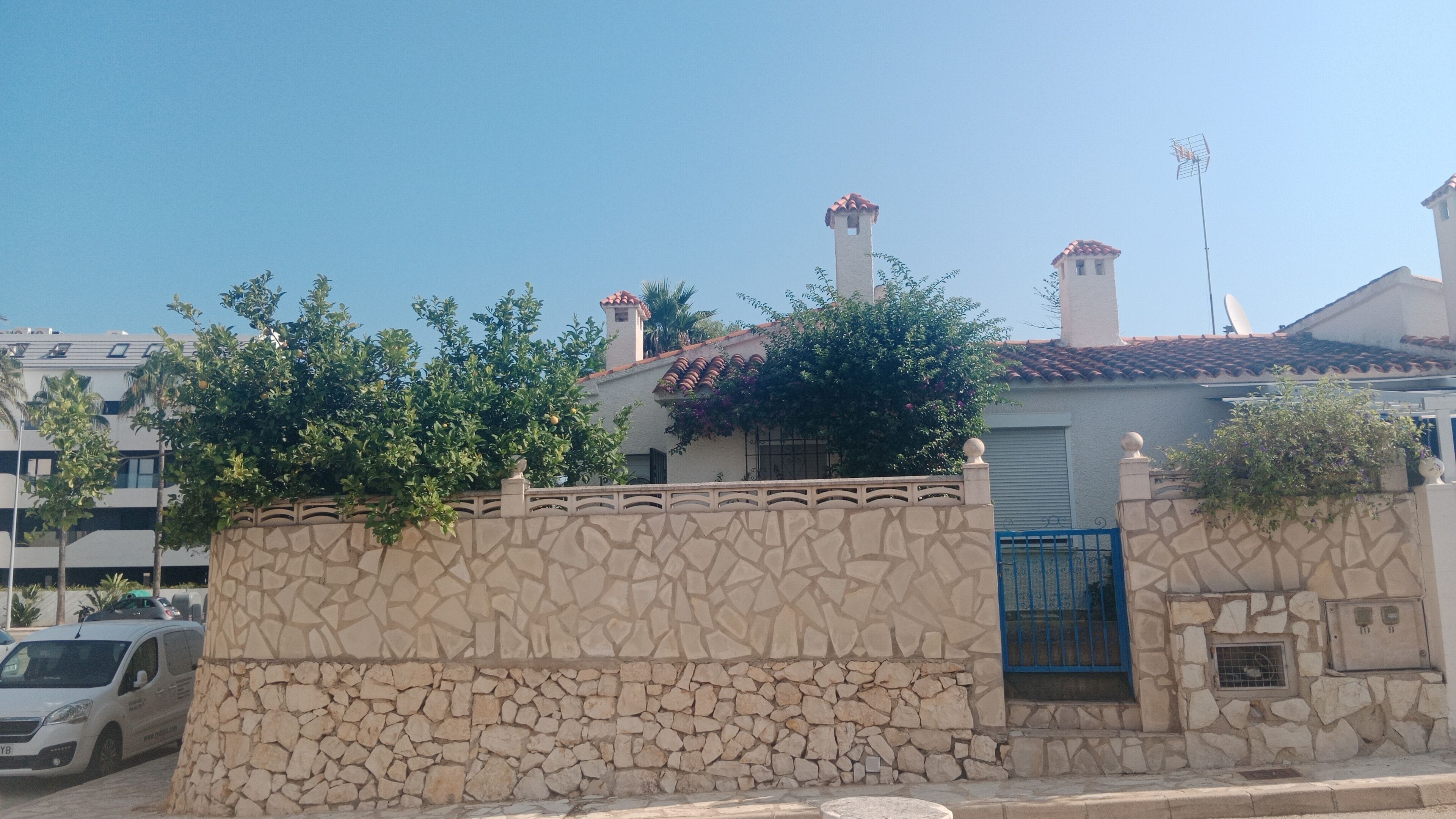 A stone wall with a gate, a building with a tiled roof, and a satellite dish.