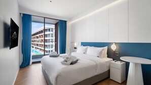 A modern hotel room with a large bed, a bedside table, a round table, and a view of a cruise ship balcony. - Premier 3-bedroom Apartment E333 Beachfront (Choeng Thale)