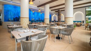 A spacious restaurant with high ceilings, large windows, and a view of an aquarium. Tables are set with chairs, and the floor is tiled. - Premier 3-bedroom Apartment E333 Beachfront (Choeng Thale)