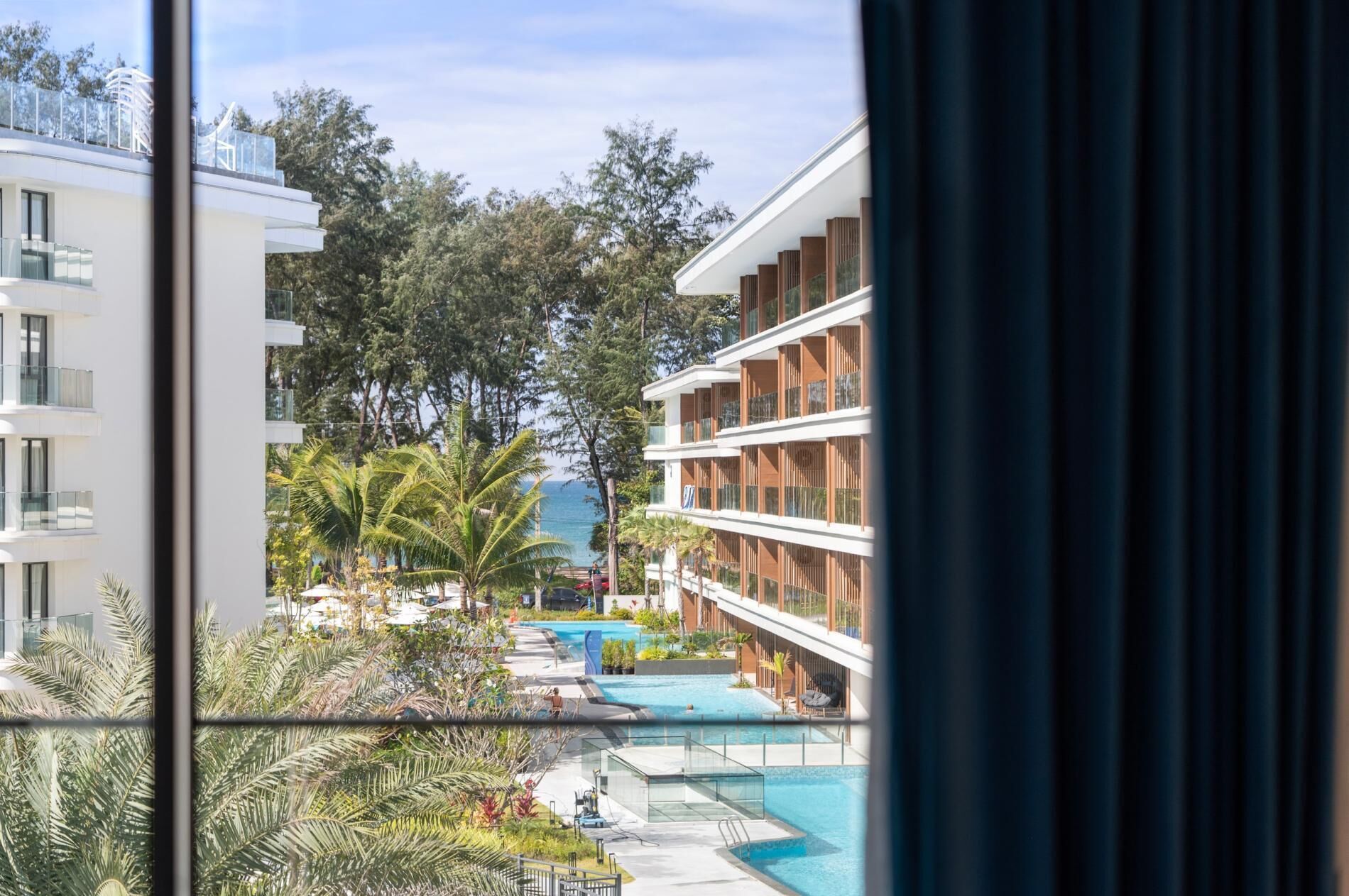A view of a hotel with a swimming pool, palm trees, and a clear sky.
